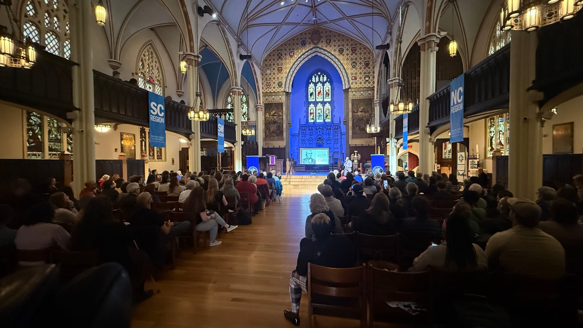 A formal keynote inside a Gothic cathedral-style venue with audience seated in pews and stage at the far end.
